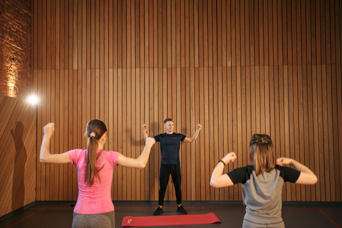 A fitness instructor leads two participants through a gym exercise.