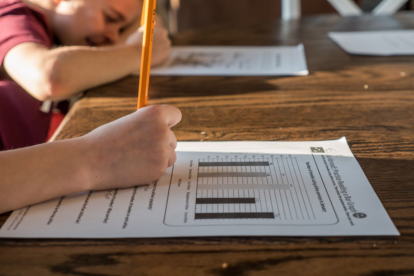 Children write on homework worksheets with pencils at a table.