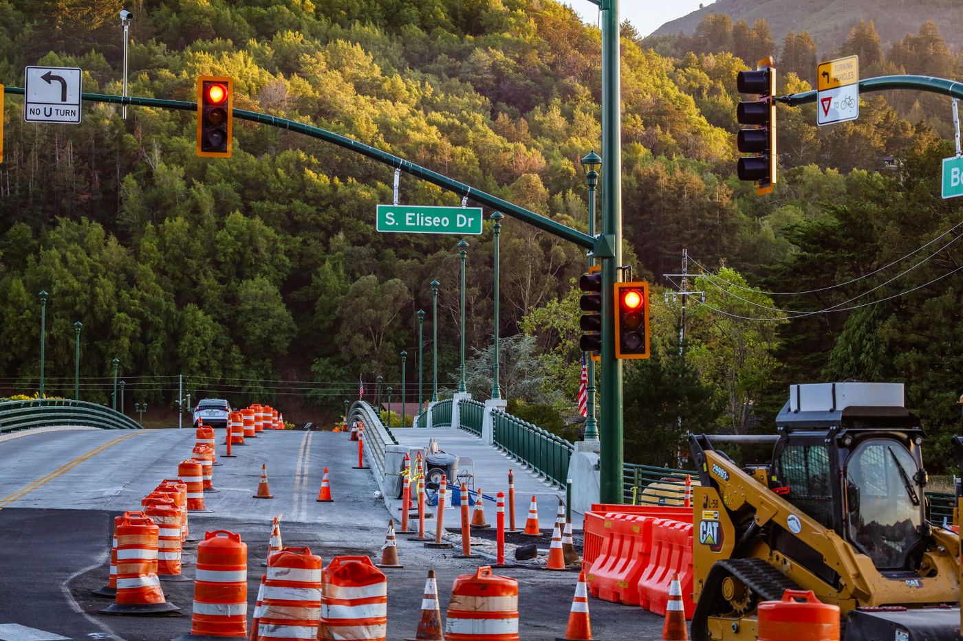 Orange traffic barrels and construction equipment line a bridge near a sign for S. Eliseo Drive.