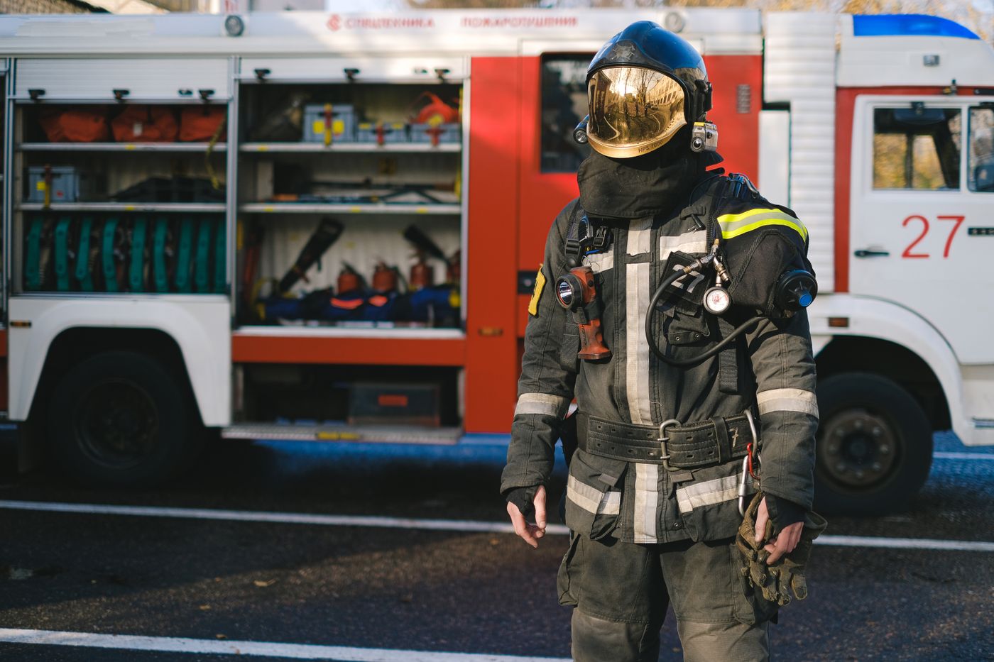 A firefighter in protective equipment stands beside a fire engine.