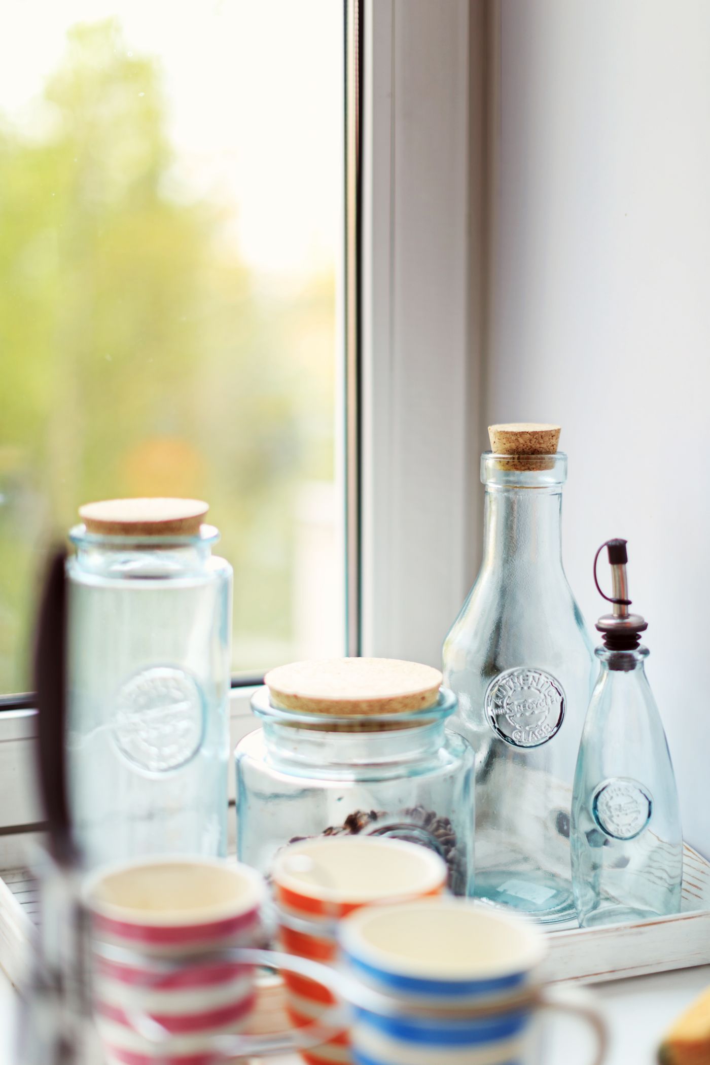Clear glass jars and bottles sit near a bright window.