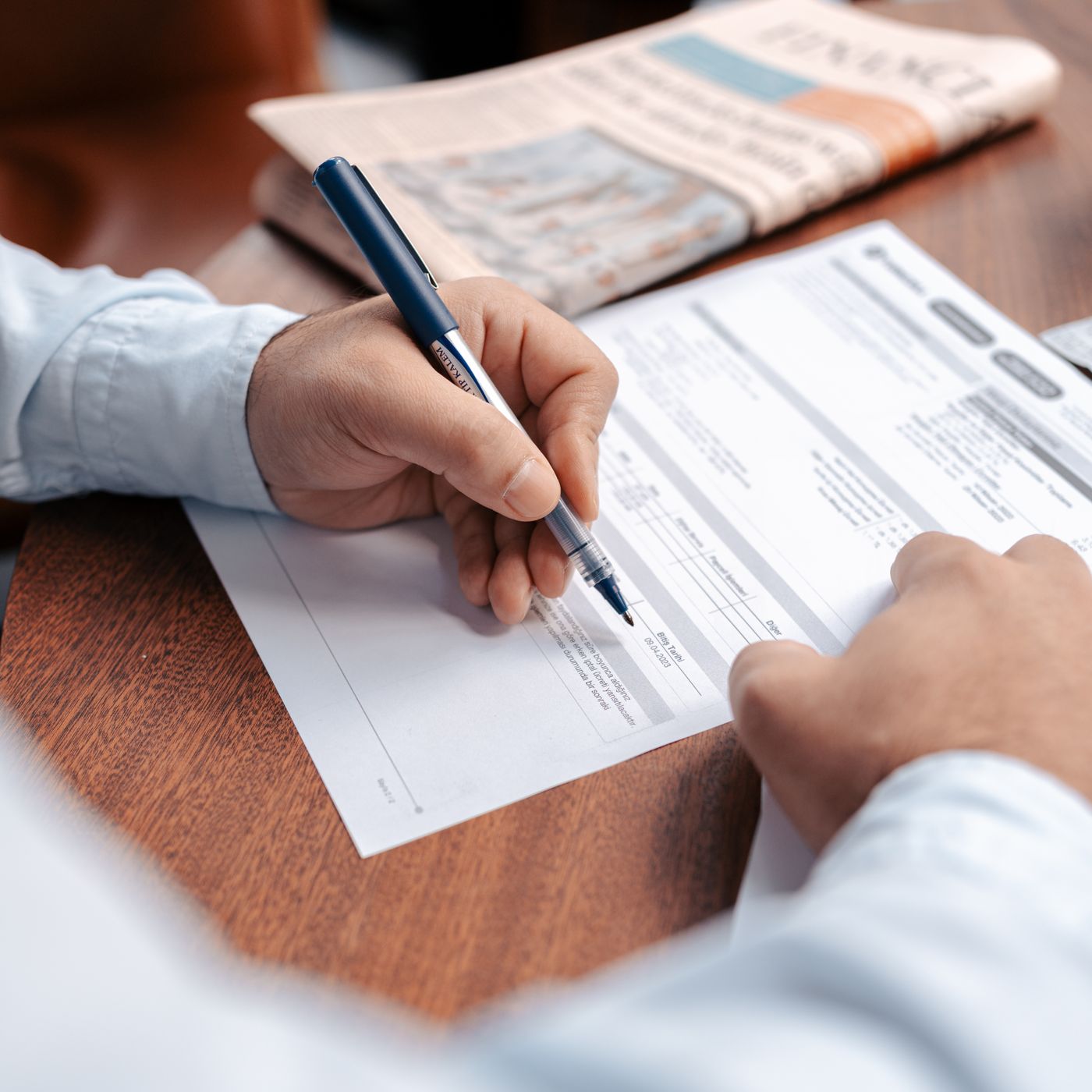 A person completes a form with a pen at a desk.