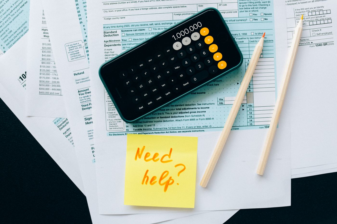A calculator phone rests on financial documents beside pencils.