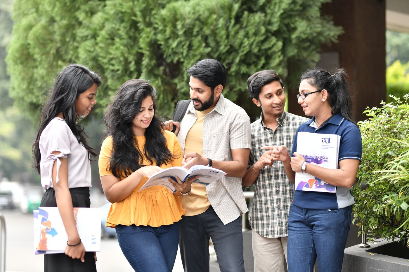 College students talk together while holding books on a campus.