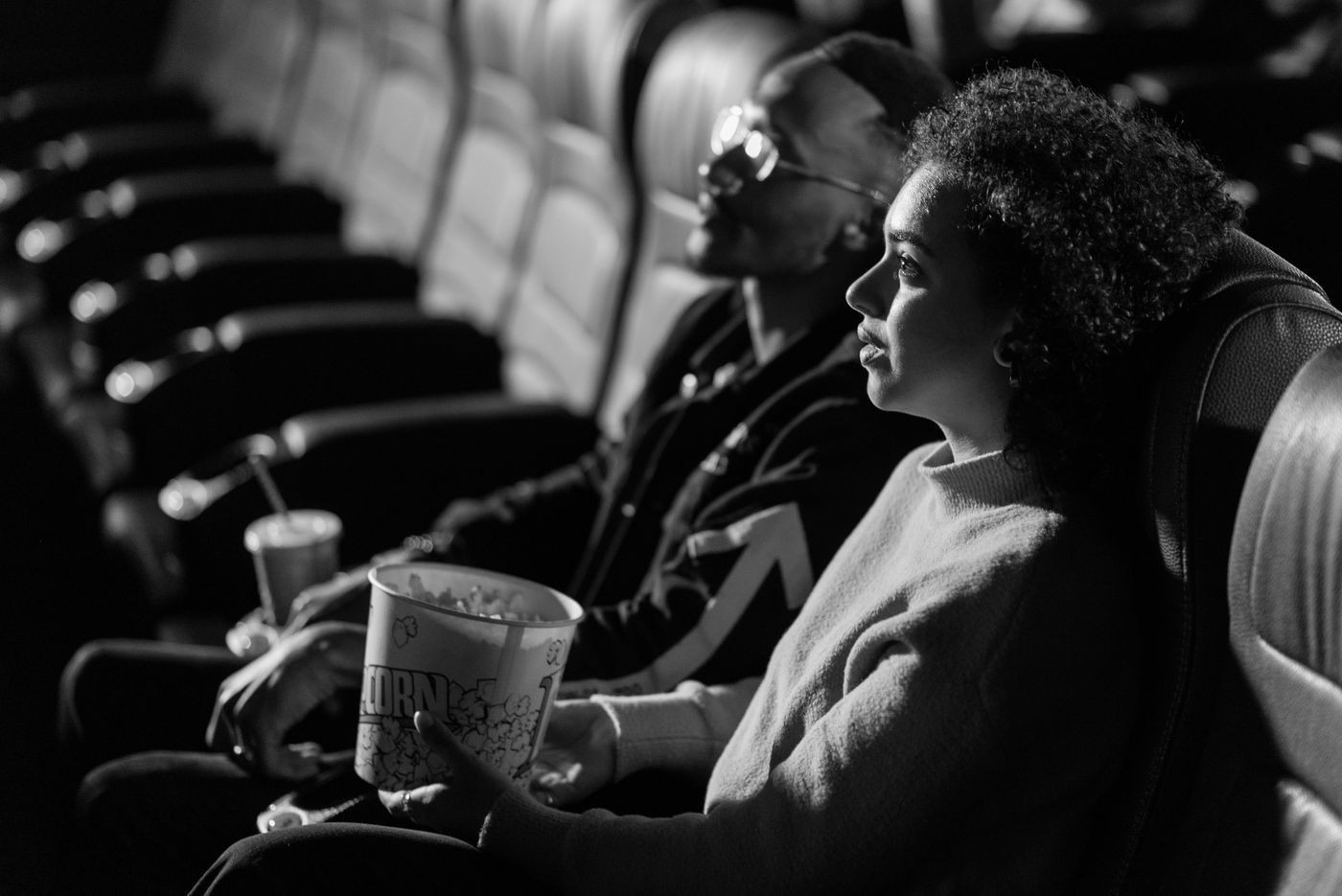 Moviegoers sit with popcorn in a dark cinema in a black-and-white photograph.