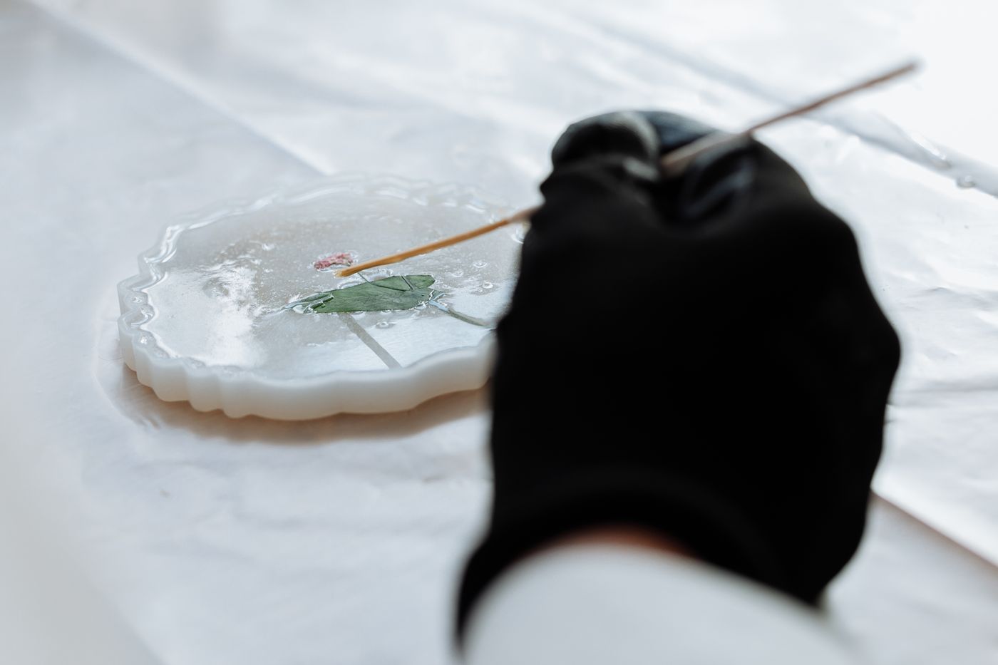 A gloved hand pours resin into a decorative mold.