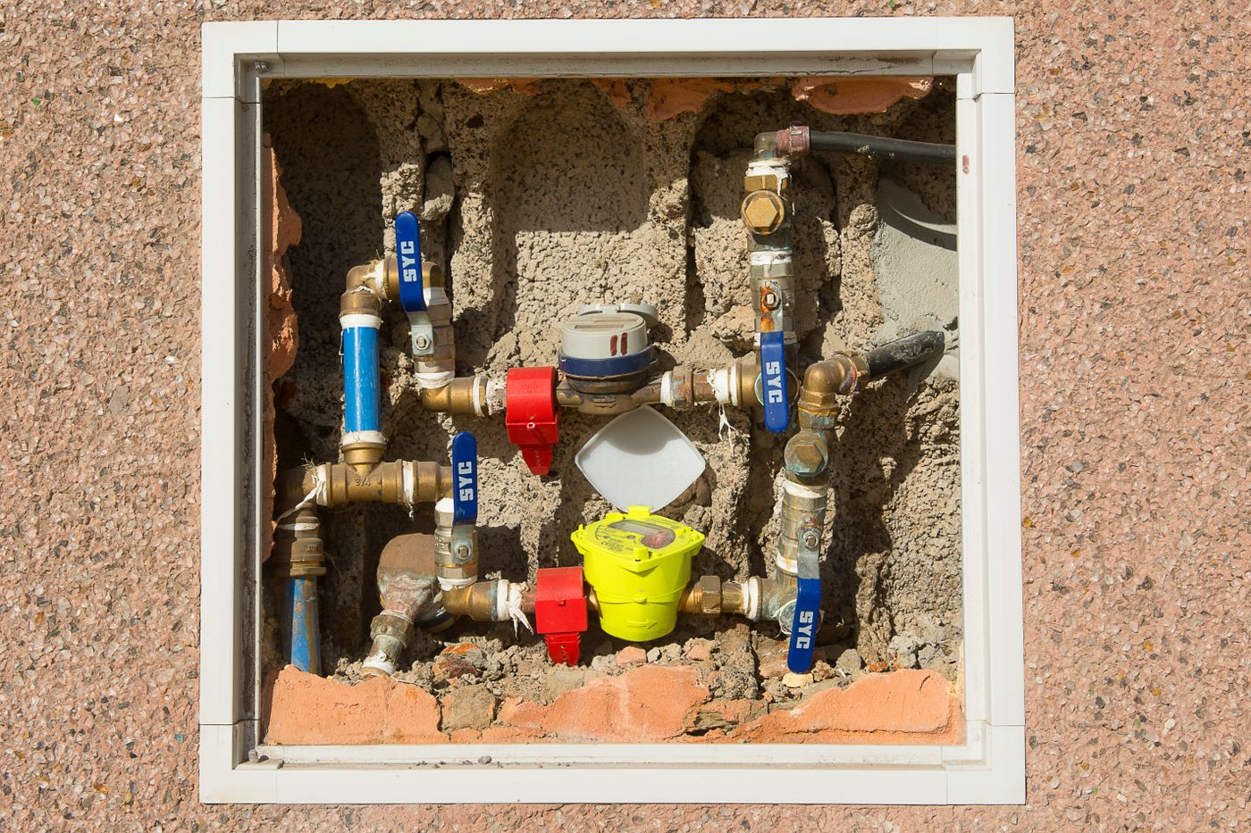 Water meters and pipes are mounted against a concrete wall.