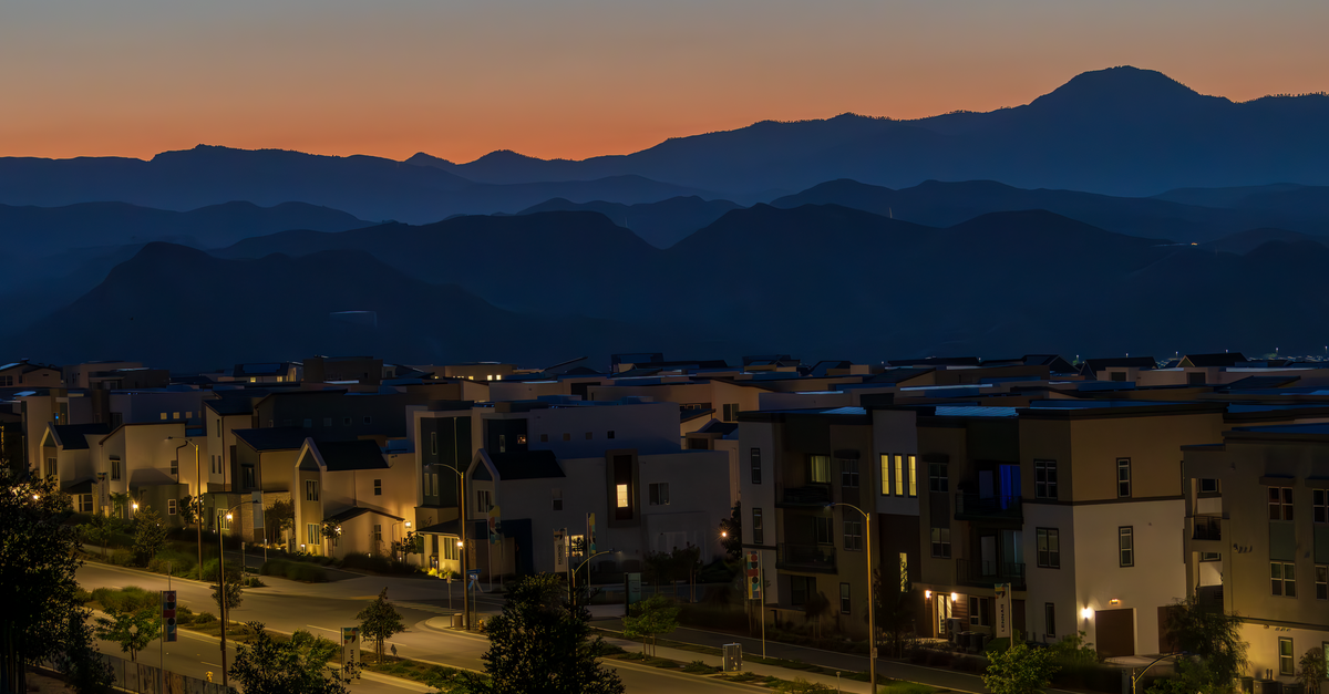 A residential neighborhood lies below a mountain ridge at dusk.
