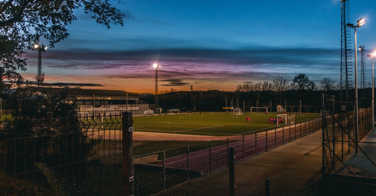 A lighted football field sits under a darkening sky.
