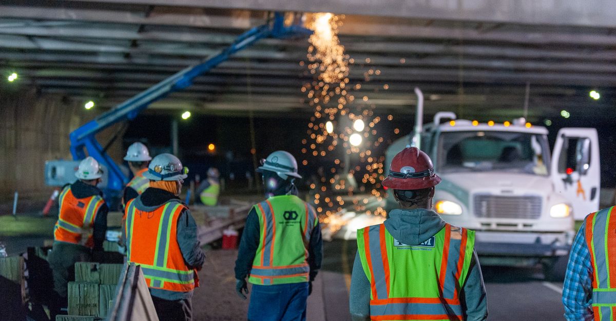 A road crew works beneath bright lights at night.