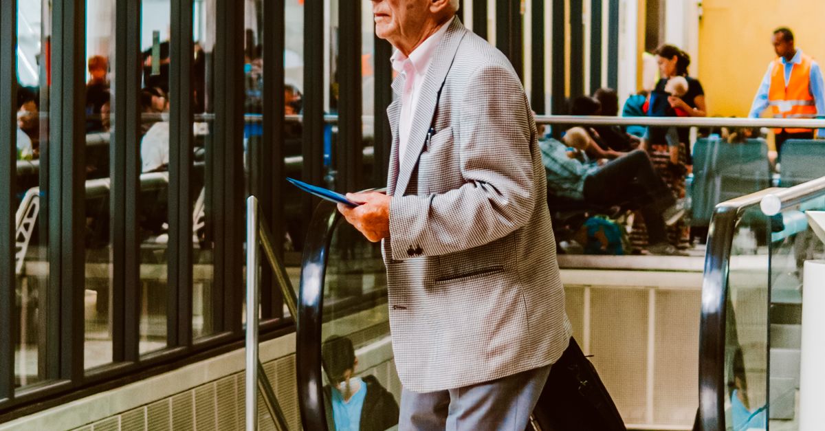A mature traveler carries luggage through an airport.