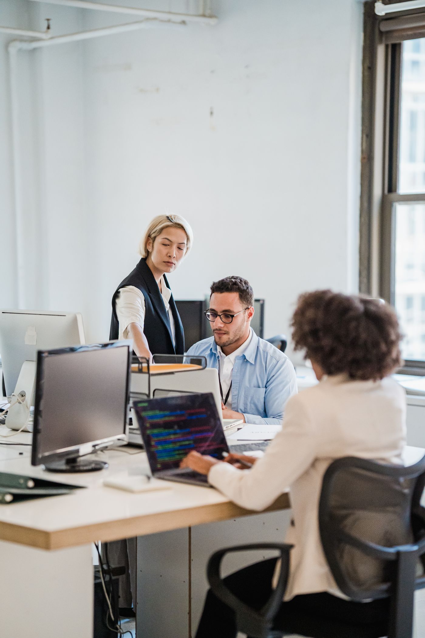 Colleagues work together around computers in a modern office.